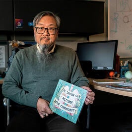 David Lo sitting at desk holding comic book. Picture taken by Kitra Cahana for Undark