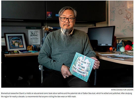 David Lo sitting at desk holding comic book. taken by Kitra Cahana for Undark