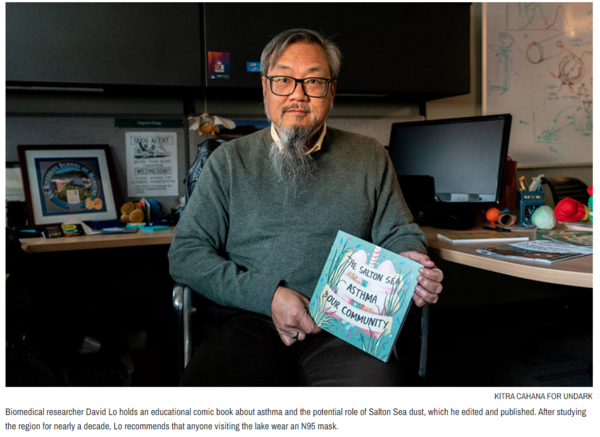 David Lo sitting at desk holding comic book. Picture taken by Kitra Cahana for Undark